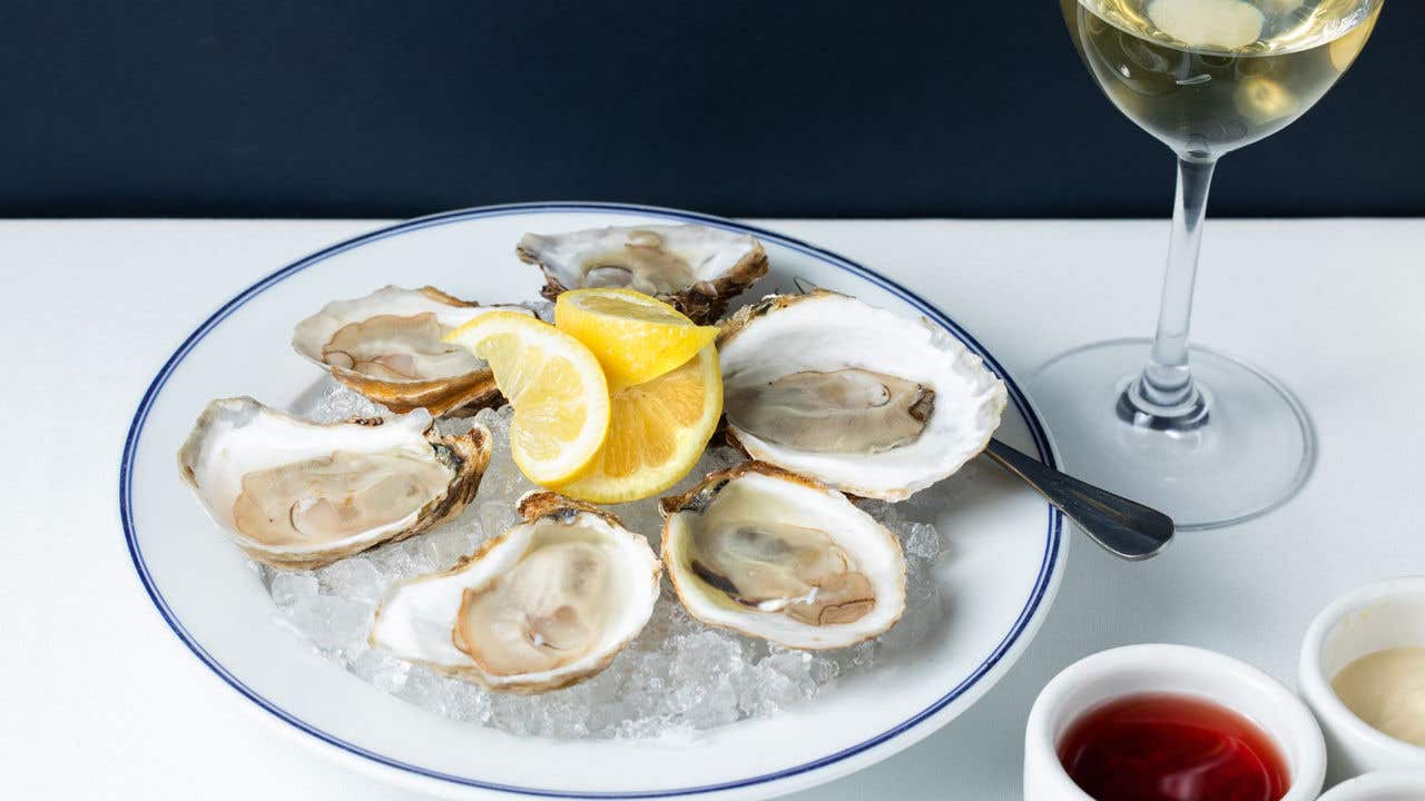Oysters on a plate with a glass of wine and dipping sauce.