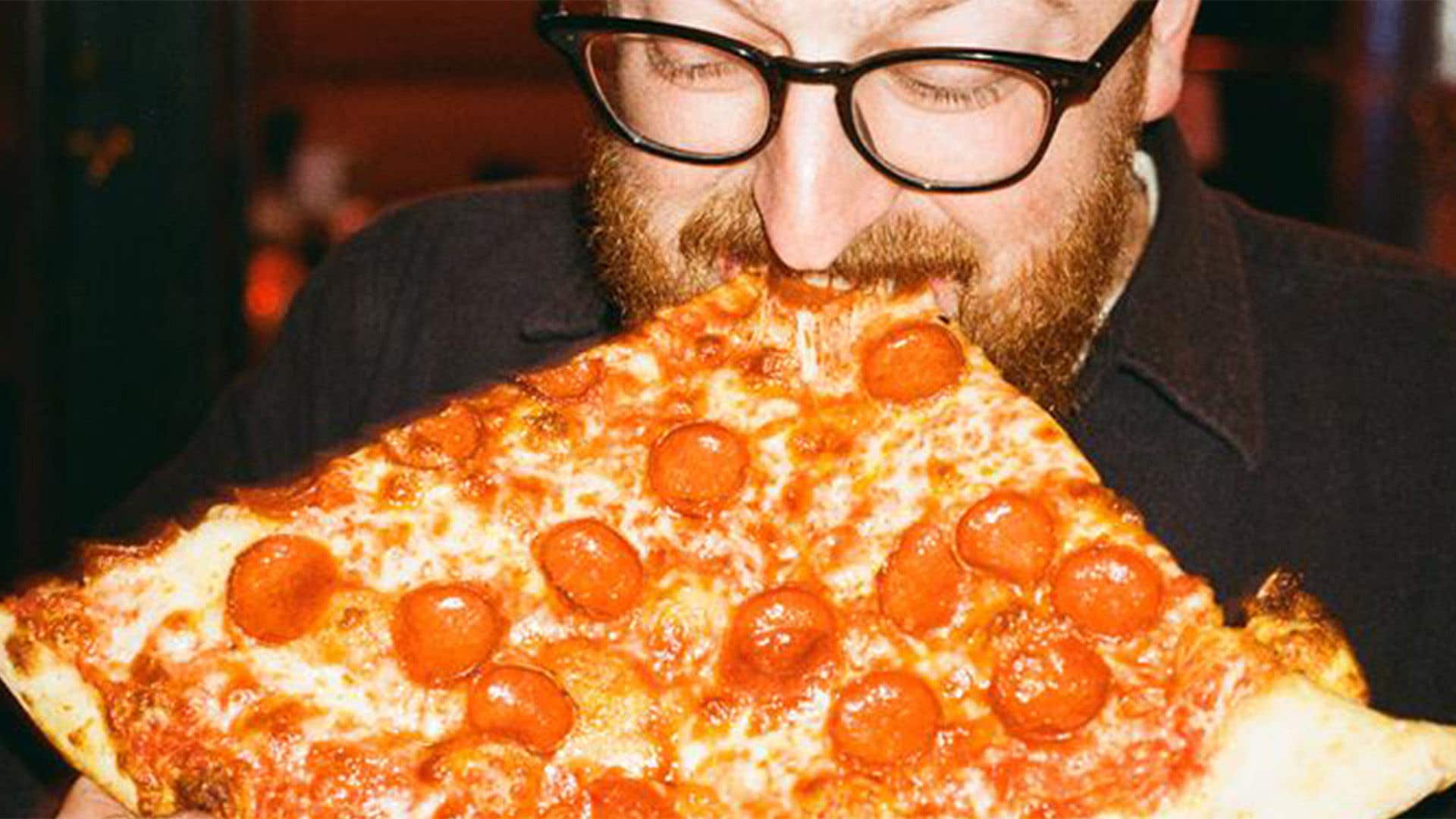 Man standing up biting into a large slice of pepperoni pizza
