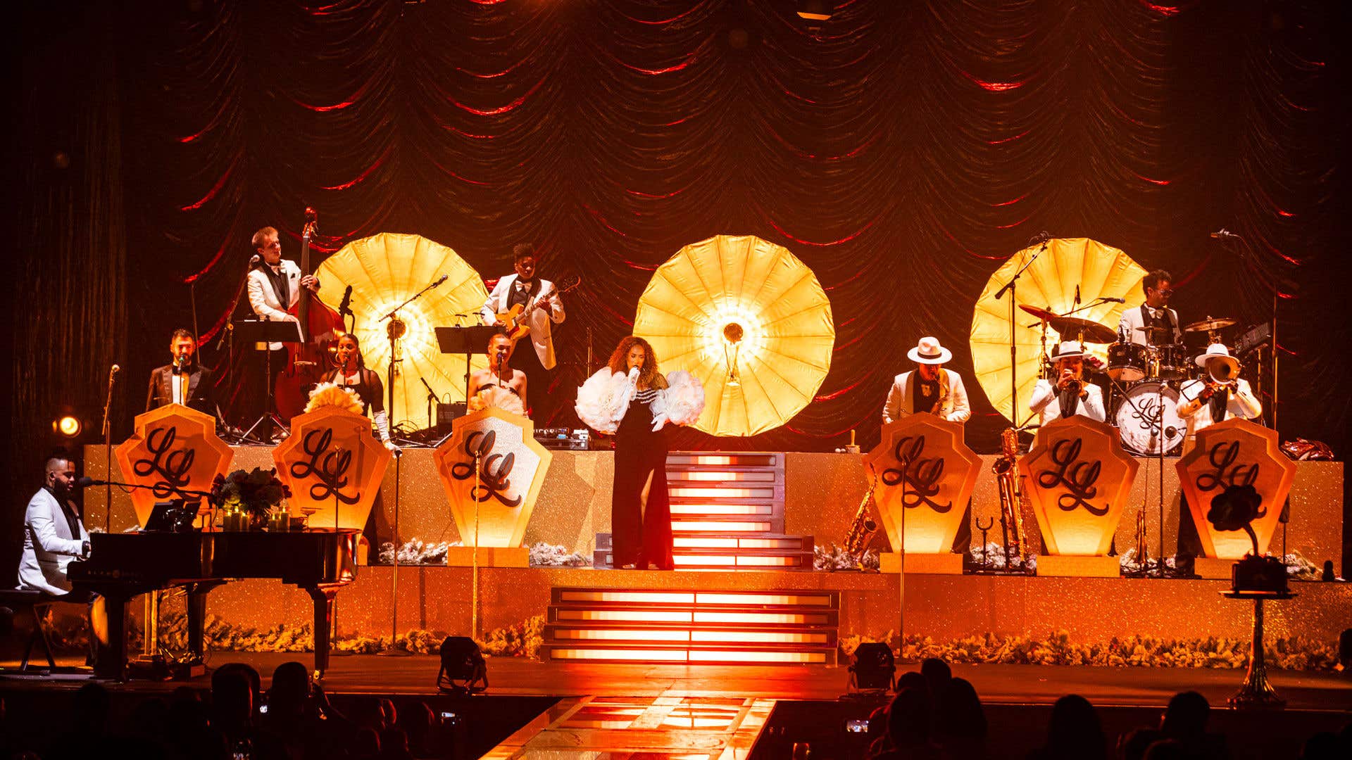 Leona Lewis on stage singing in a black gown with white puffy sleeves. 
