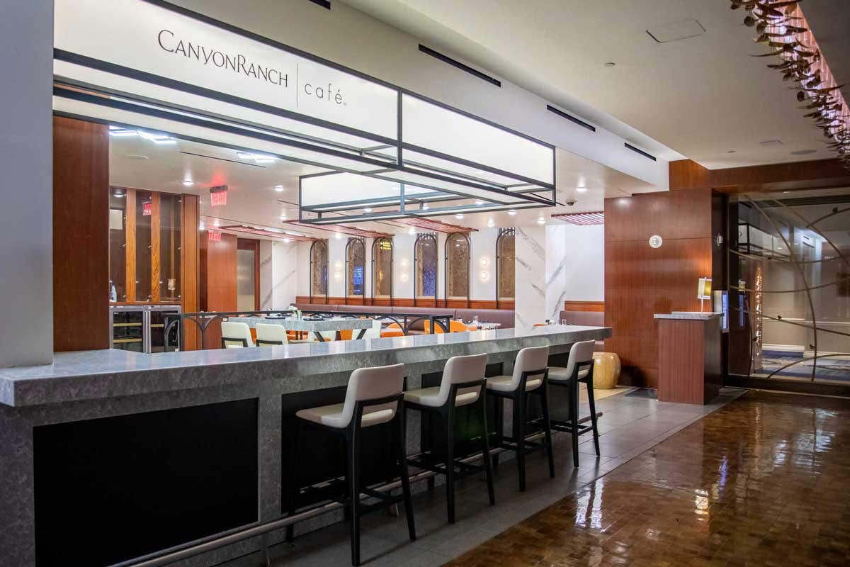 Restaurant with a bar and high-top chairs in front of a dining room.