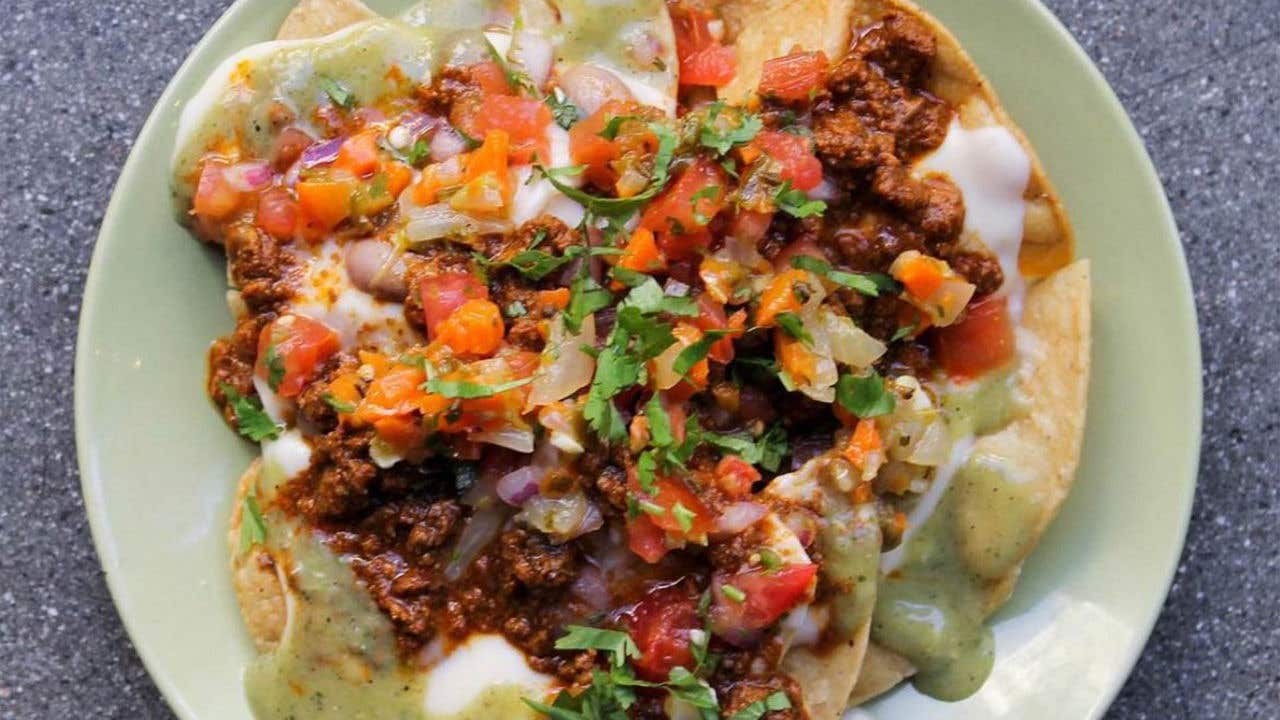 Tortilla chips covered with meat, cheese and salsa on a plate.